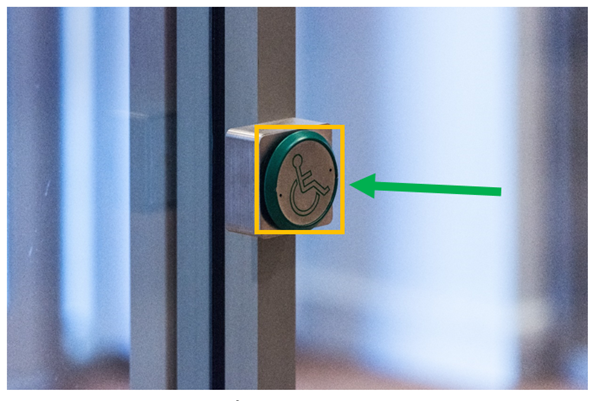 External door open button on porch door frame. This image shows the external door open button for exiting onto the street if assistance with opening the door is required. Assistance can also be sought from staff or security staff.This image also shows the button highlighted by a yellow box and a green arrow pointing to the yellow box.