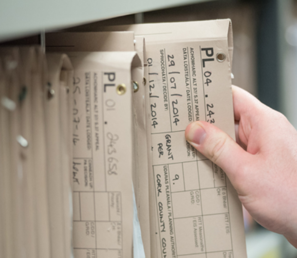 A close-up shot of a hand pulling a labeled, tan-colored planning file from a metal shelf.